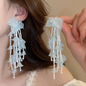 Gros plan de boucles d'oreilles pampilles feuilles bleu clair avec perles et aiguille en argent.