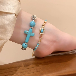 Detail of beaded turquoise bracelet with cross charm and delicate gold chain set