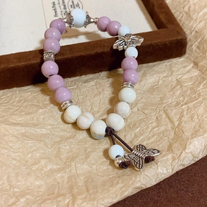 Detailed shot of ceramic beads with silver butterfly and flower charms on a woven bracelet
