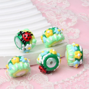 Macro detail of green glass beads with 3D ladybug and floral patterns for DIY jewelry