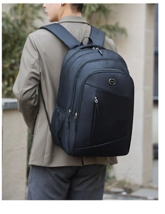 Rear view of a black multi-compartment business backpack worn outdoors showing padded straps