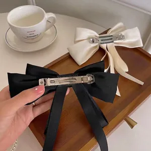 Elegant satin bow hair clips in black and beige on a vintage wooden tray setup