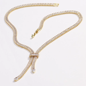 Collana a V dorata alla moda con pietre di zircone e nappine su sfondo bianco puro