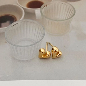 Macro shot of gold heart stud earrings on a white surface with elegant background