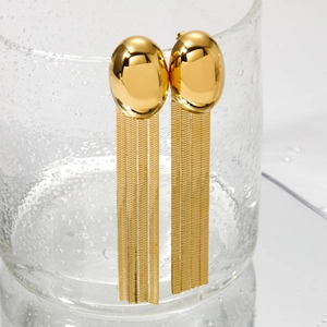 Boucles d'oreilles à pompons en acier inoxydable doré accrochées sur un verre d'eau