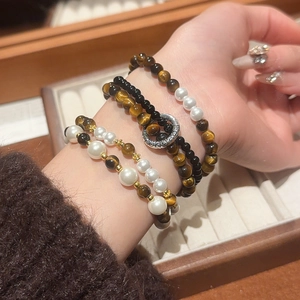Close-up of stacked tiger eye and pearl beaded bracelets on a vintage leather background