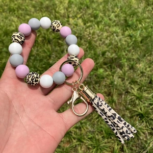 Dettaglio del bracciale portachiavi con perle di silicone e nappa leopardata su erba verde