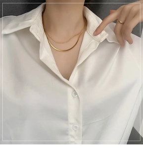 Close-up of layered gold snake chain and beaded necklace on white silk shirt