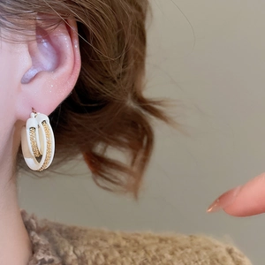 Macro detail of 18k gold plated C-shape hoop earrings with white enamel and metal chain inlay