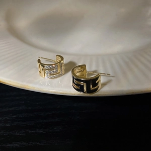 Détail de boucles d'oreilles créoles C en or avec strass et incrustation d'émail noir