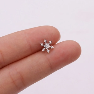 Macro detail of a silver snowflake stud earring with micro-paved zircons on a fingertip