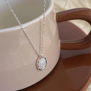 Close-up of minimalist silver opal necklace hanging on the rim of a beige ceramic coffee cup