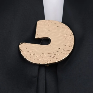 Détail macro d'une broche dorée à texture martelée sur un tissu en soie noire
