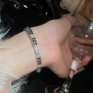 Close-up of silver-tone zirconia rivet bangle on wrist in a luxury social setting