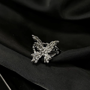 Detailed close-up of textured butterfly ring on premium black silk fabric background