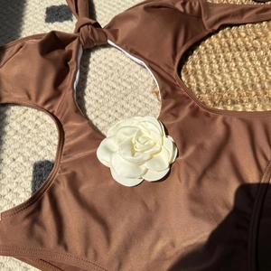 Detailed close-up of dark brown swimsuit with elegant 3D white satin flower and lace-up ties
