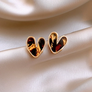 Macro shot of gold heart-shaped leopard print earrings on soft champagne silk fabric