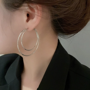 Close-up of model wearing double-layered silver hoop earrings in polished metal finish
