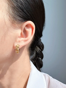 Detailed close-up of textured gold ribbon-style hoop earring worn on a person