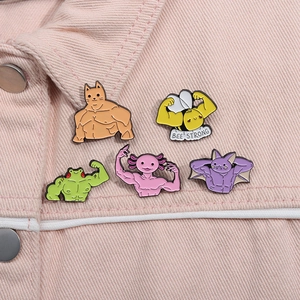 Detail of five cartoon gym animal enamel pins on pink denim fabric with Bee Strong slogan