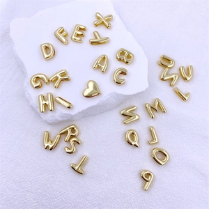 Close-up of golden alphabet charms and heart beads on white textured surface for DIY bracelets