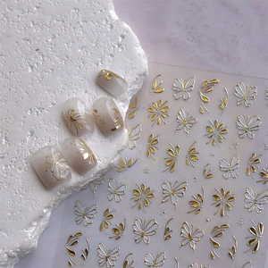 Detailed view of gold foil butterfly and flower nail art stickers on milky white nails