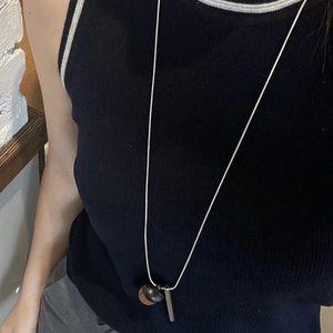 Close-up of acorn pendant and silver bar on long snake chain over black rib top