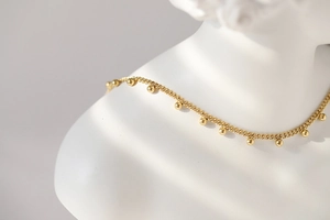 Macro detail of gold beaded lace chain necklace on a minimalist white sculpture base
