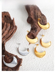 Présentation artistique de boucles d'oreilles croissant dorées et argentées sur bois naturel