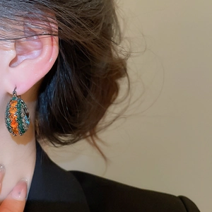 Nahaufnahme von Vintage-Ohrringen mit orangefarbenen und grünen Steinen am Modell