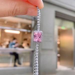 Close-up of silver chain with square pink gemstone pendant held in hand for detail