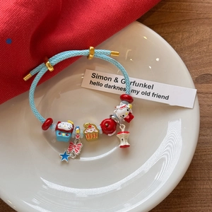 Détail du bracelet en corde tressée bleu clair avec charms de chat de dessin animé et pomme
