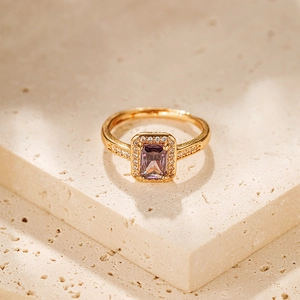 Close-up of adjustable gold ring with emerald-cut purple gemstone on textured stone