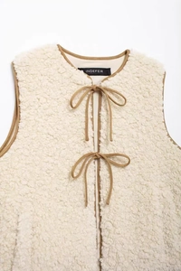 Detail of cream fleece vest featuring soft texture and double bow-tie ribbon closures