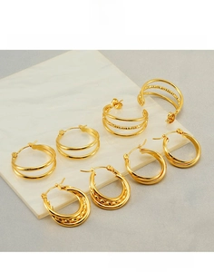 Macro shot of tiered gold titanium steel hoop earrings on white marble texture surface