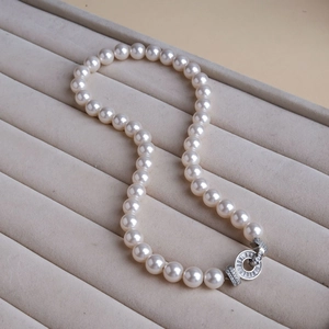 Detail of white round pearl necklace featuring a sparkling zircon studded silver clasp
