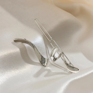 Macro detail of silver wavy metal hairpin with a polished finish on champagne silk fabric