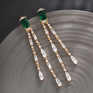 Detail of luxury emerald green teardrop tassel earrings on a textured ceramic tray