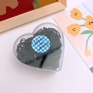 Macro view of black elastic hair bands stored in a heart-shaped clear plastic box