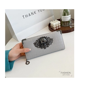 Detail of gray crocodile pattern long wallet featuring a large metal skull buckle and ring zipper