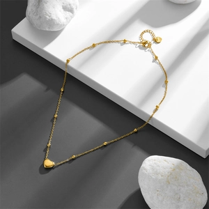 Minimalist gold heart pendant necklace with small bead accents on a geometric display