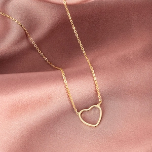 Close-up of minimalist 18k gold heart pendant on a thin O-chain over silk fabric