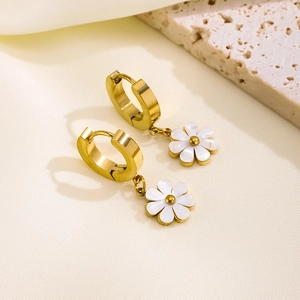 Golden daisy hoop earrings set with white floral pendants on a minimalist stone background