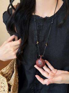 Detailed close-up of dark wood heart gourd pendant with vintage metal floral emblem