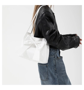 Detail of a large white tote bag featuring a prominent oversized bow design and slim straps