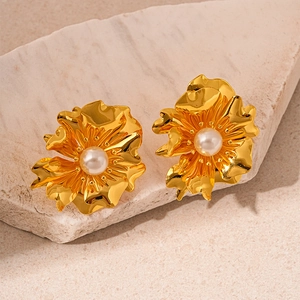Close-up of golden wavy floral earrings with a central pearl on a textured stone surface