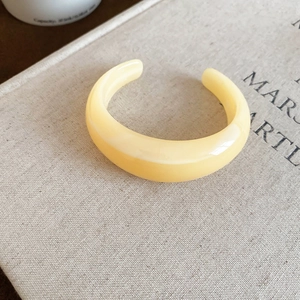 Gros plan détaillé du bracelet jonc large blanc crème sur fond de livre en lin minimaliste