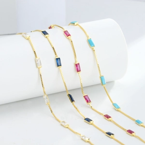 Detailed close-up of delicate gold box chains featuring colorful baguette-cut gemstones