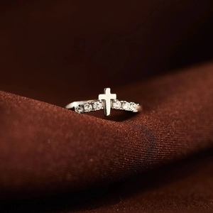 Close-up of silver cross ring with cubic zirconia stones on brown satin background