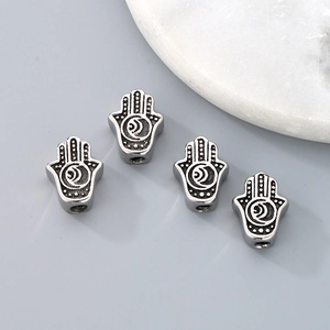 Macro detail of four silver Hamsa hand beads with engraved moon and star patterns